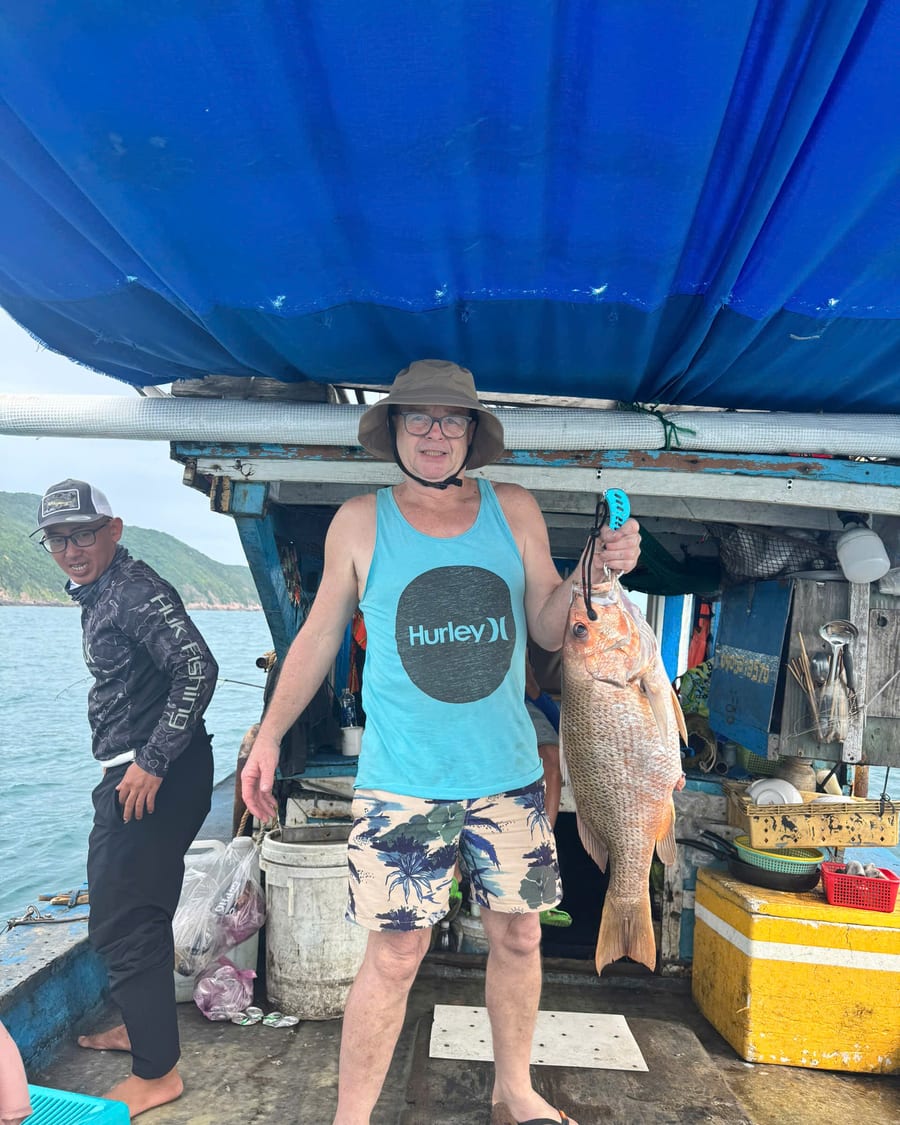 Crew member and guest with a snapper under the boat canopy